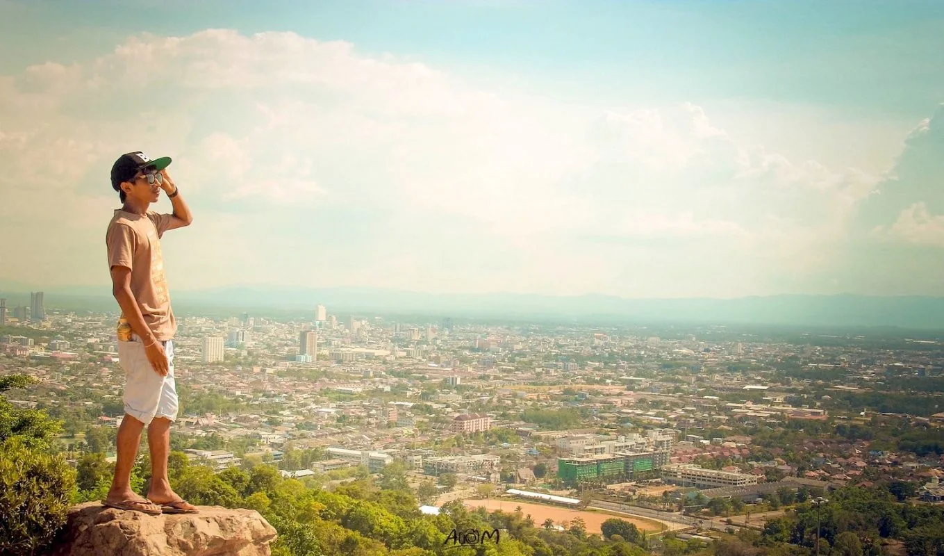 Man looking out over the Chiang Mai valley from a mountain viewpoint at golden hour